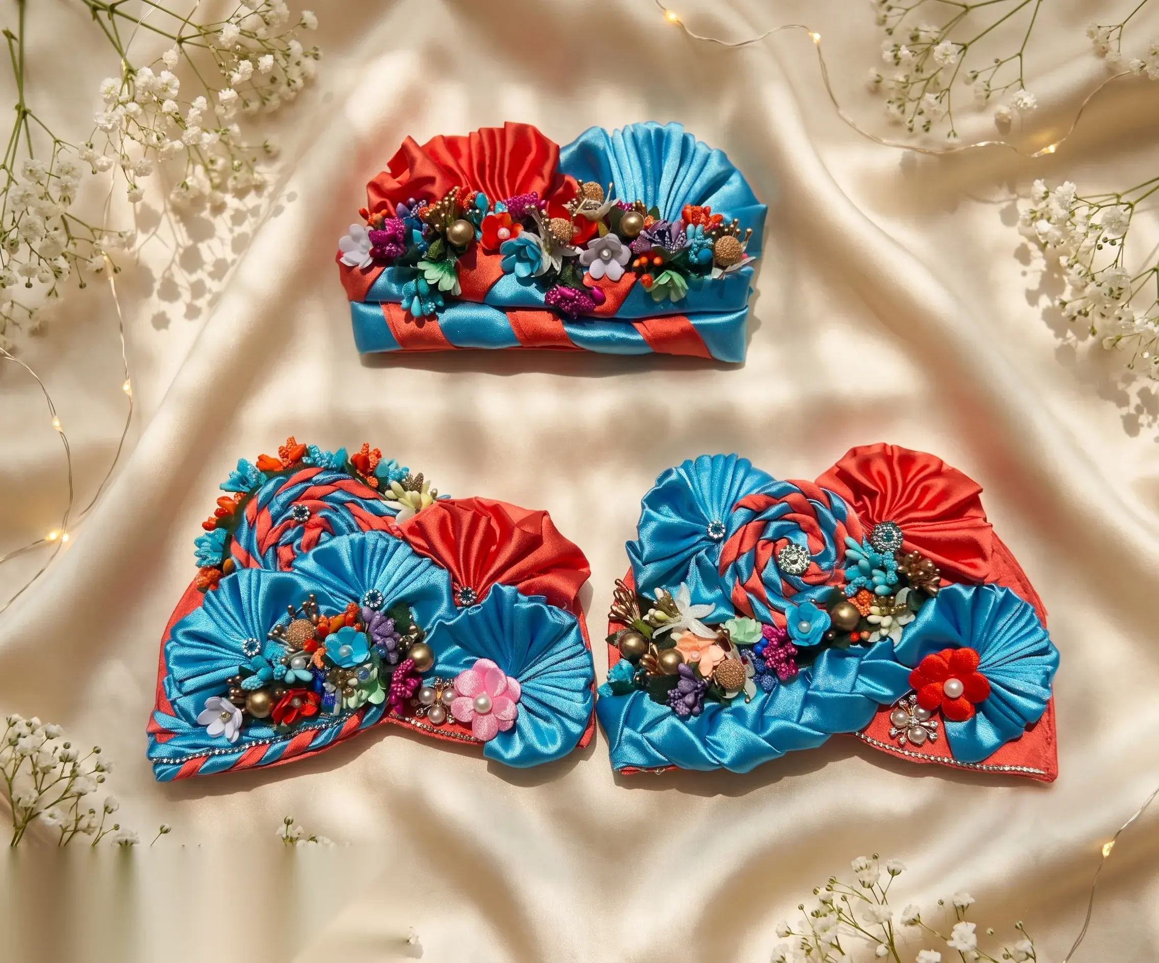 Three fan-pleated satin mukuts in teal and coral decorated with fabric flowers, beads, and gold accents.